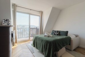 Ein Schlafzimmer mit einem Bett, einem Sofa, einem Fenster mit Vorhängen und Blick ins Freie.