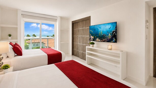 A hotel room with two beds, a TV, a window with a view of the beach, and a plant on the nightstand. - Villa Riviera Luxe, Coastal 4BR Retreat in Miami (Miami)