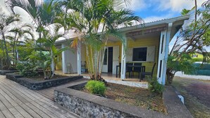 Una casa con porche, mobiliario exterior y un jardín con plantas y una terraza de madera.