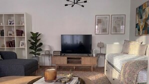 A modern living room with a flat-screen TV, a bookshelf, a coffee table with a book, and a large plant.
