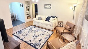 En stue med en hvid sofa, et sofabord, en beige lænestol, en gulvlampe og en loftventilator.