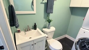 Et badeværelse med en hvid vask, spejl, toilet og vaskemaskine.