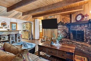 Un interior rústico con techo de madera, chimenea, televisor de pantalla plana y un rincón de estar acogedor con un tapiz estampado.