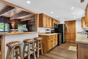 Una cocina con armarios de madera, un refrigerador, un microondas y una barra con taburetes.