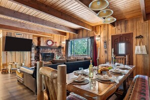 Interior de madera con chimenea, zona de estar y mesa de comedor preparada para una comida.