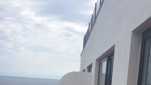 Ein Balkon mit Tisch und Stühlen, einem weißen Geländer und Blick auf das Meer.