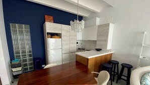 Eine moderne Küche mit einem Holzespeisetisch, weißen Stühlen, einer Pendelleuchte und einer integrierten Kücheninsel mit Hockern.