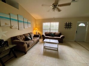 A living room with two sofas, a coffee table, a ceiling fan, and artwork on the wall. - 3-bedroom pool house in SW Cape Coral - pet friendly with fenced backyard (Cape Coral)