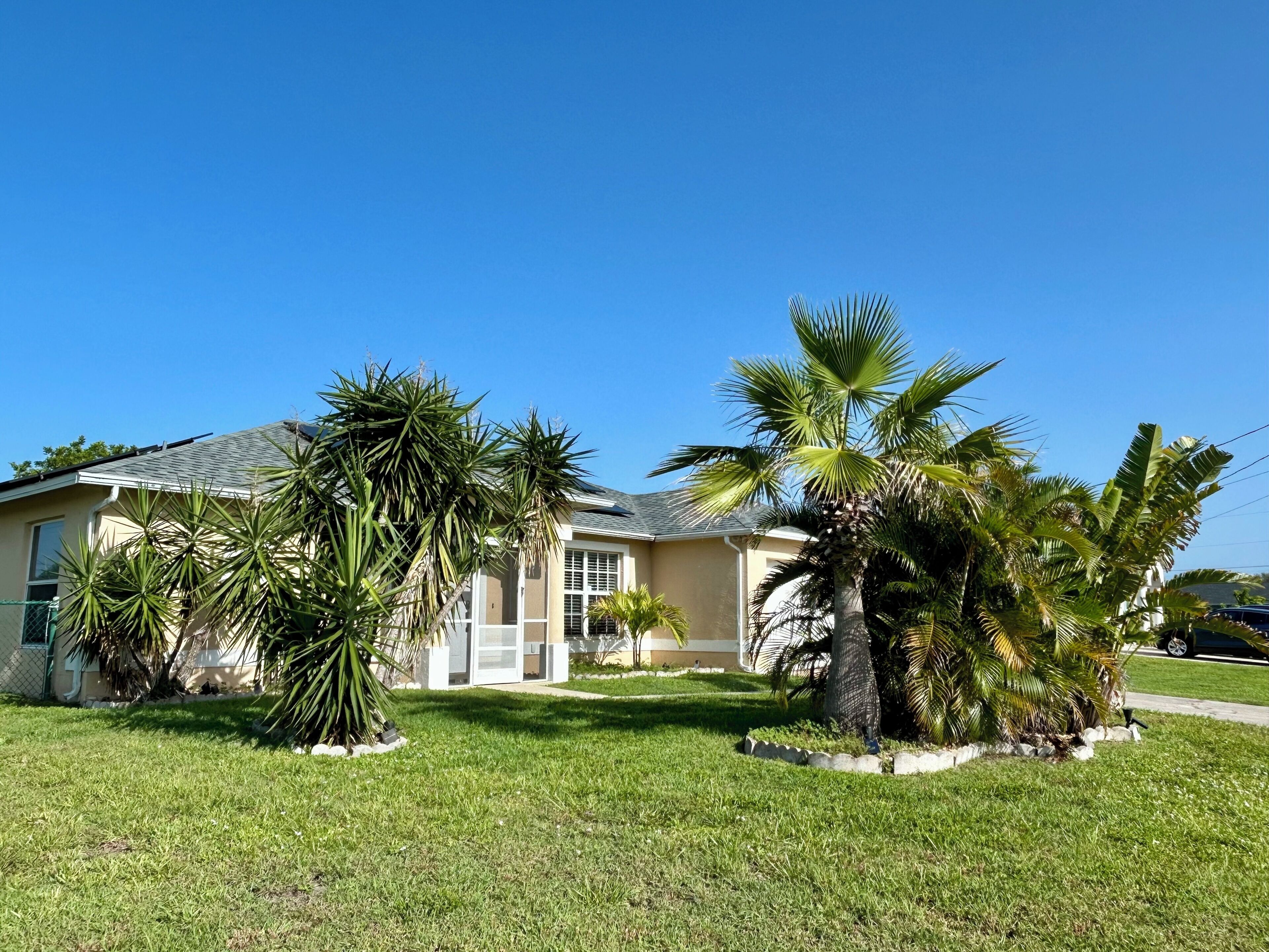 A residential house with a well-maintained lawn, palm trees, and a garage.