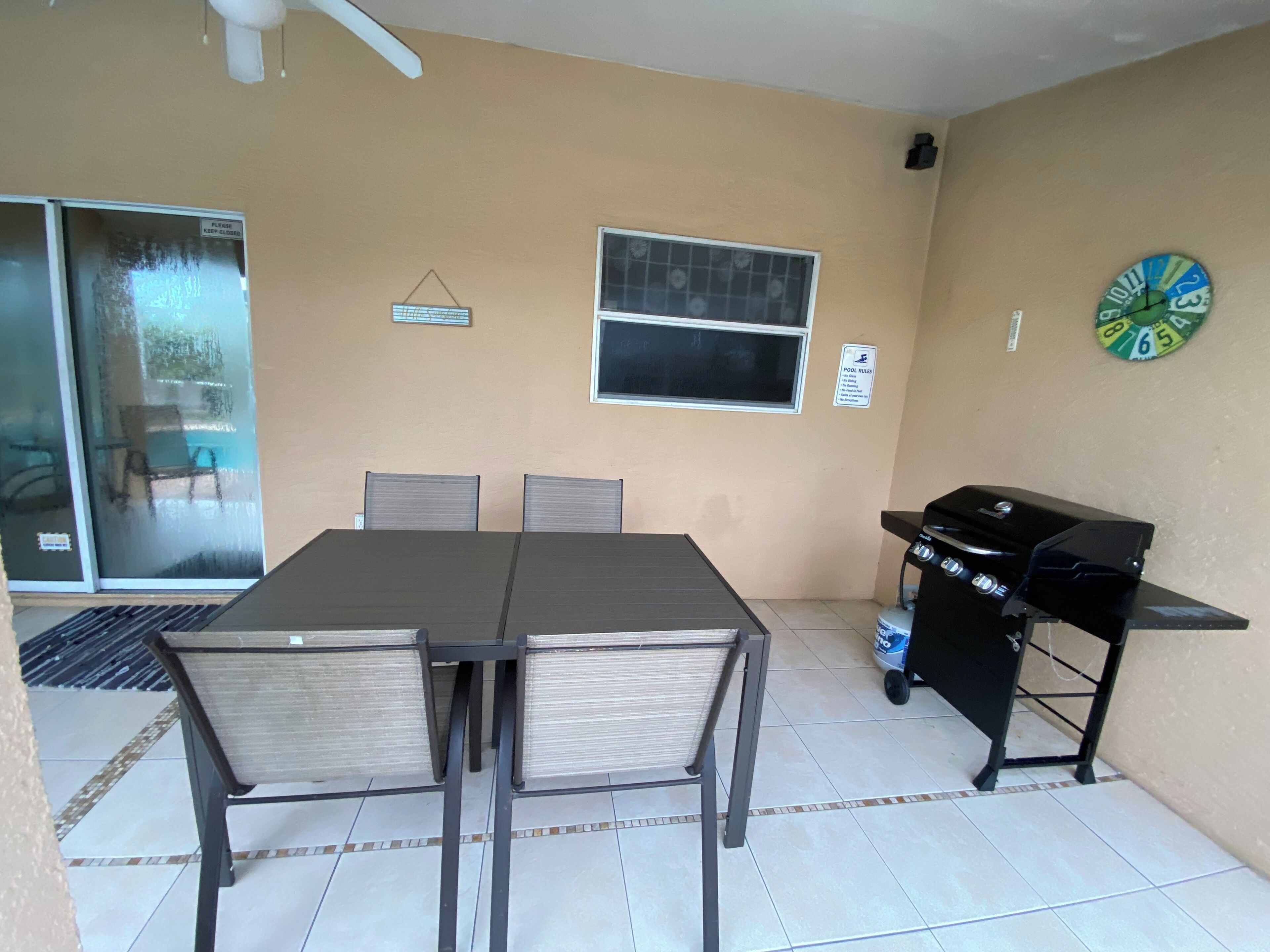 Uma área de pátio com mesa, cadeiras, churrasqueira e uma janela com uma placa.