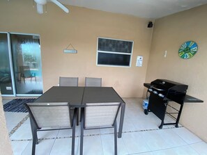 A patio area with a table and chairs, a grill, and a window with a sign. - 3-bedroom pool house in SW Cape Coral - pet friendly with fenced backyard (Cape Coral)