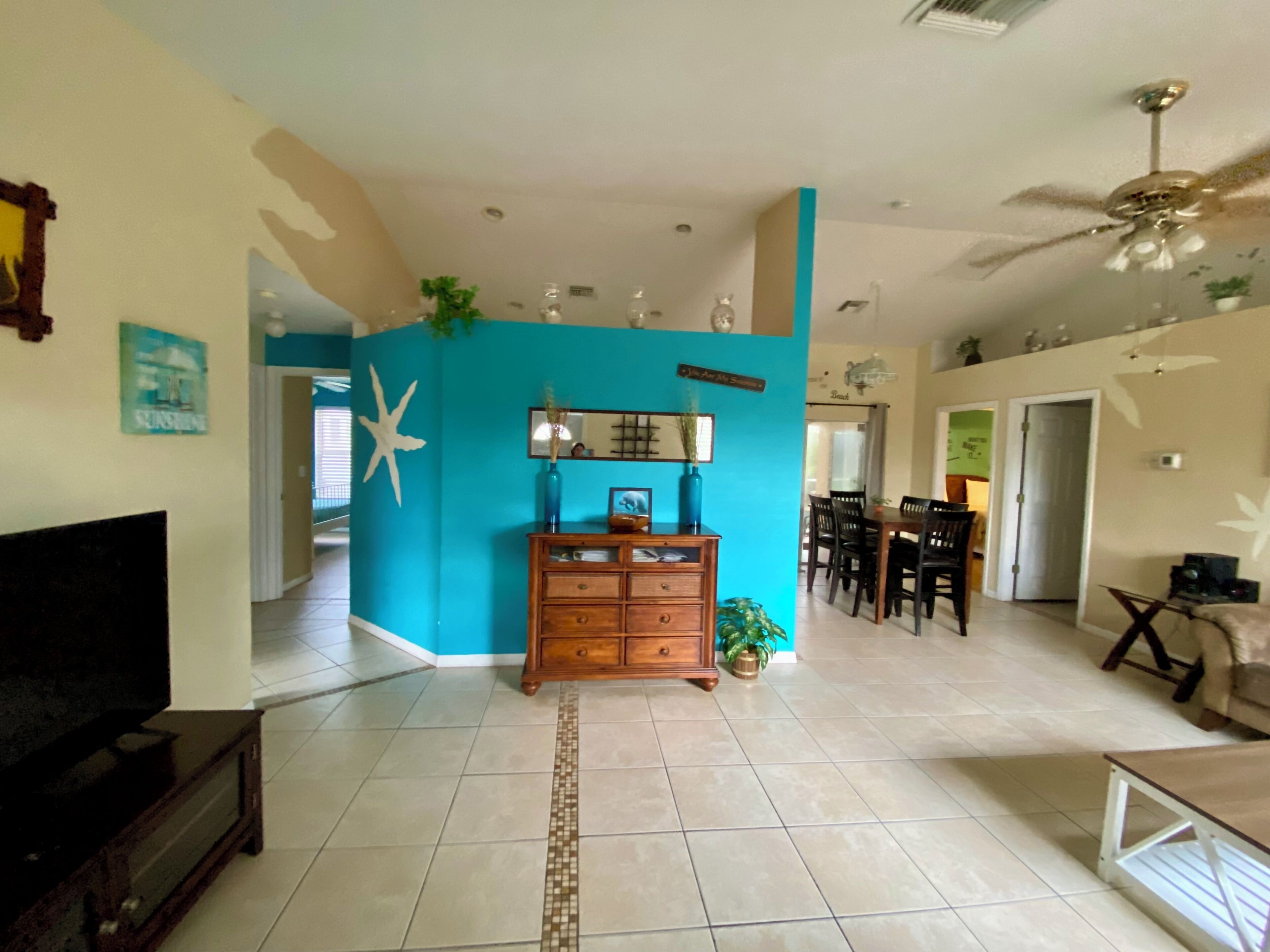 A spacious living room with a wooden cabinet, a dining area with chairs, and a ceiling fan.
