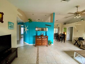 A spacious living room with a wooden cabinet, a dining area with chairs, and a ceiling fan. - 3-bedroom pool house in SW Cape Coral - pet friendly with fenced backyard (Cape Coral)