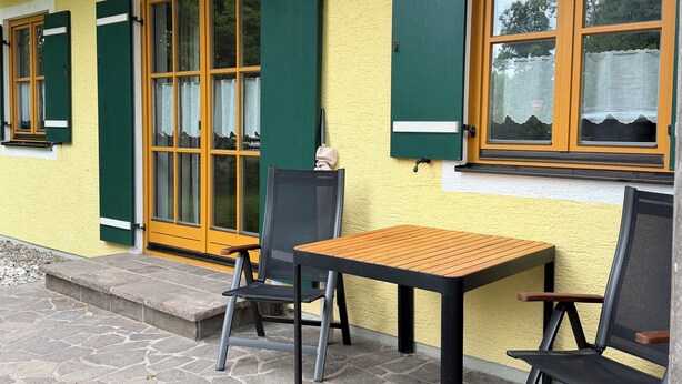 Un edificio amarillo con contraventanas verdes, una mesa de madera y dos sillas.