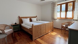 Un dormitorio con cama de madera, mesita de noche, silla de mimbre, ventana con cortinas y ventilador de techo.