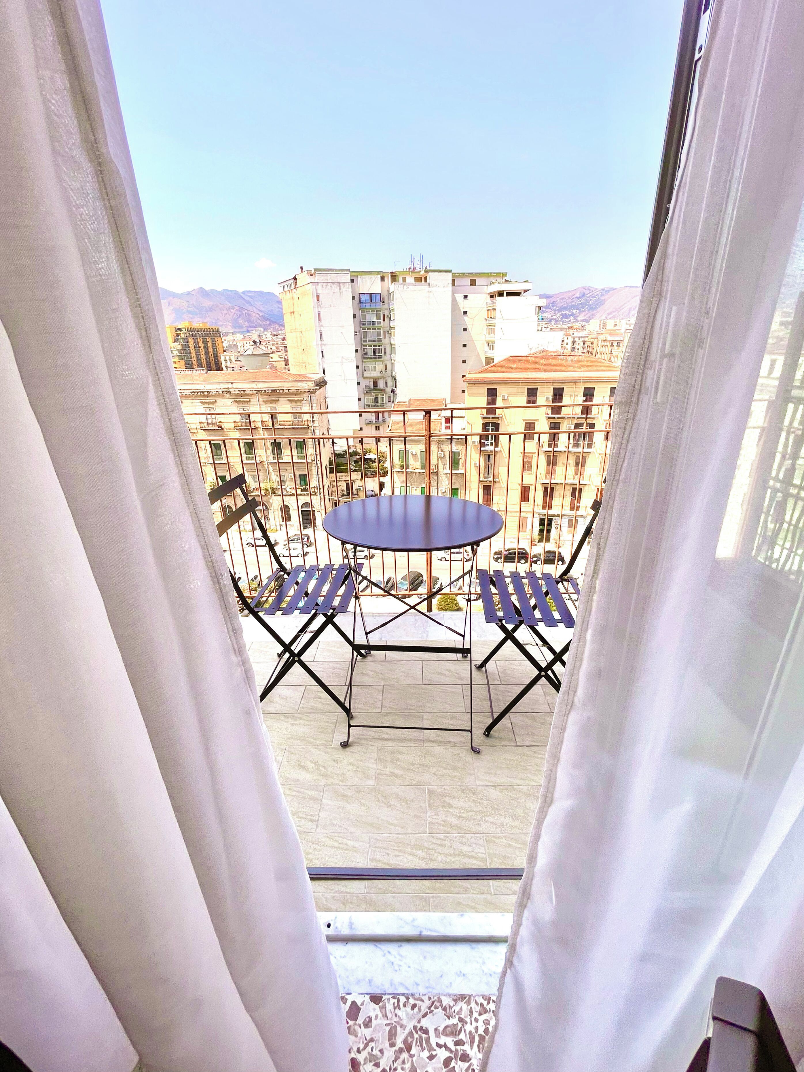 Een balkon met een tafel en stoelen, met uitzicht op een stadsgezicht met gebouwen en bergen.