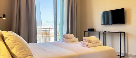 A hotel room with a bed, a TV, a table, and a view of the outdoors.