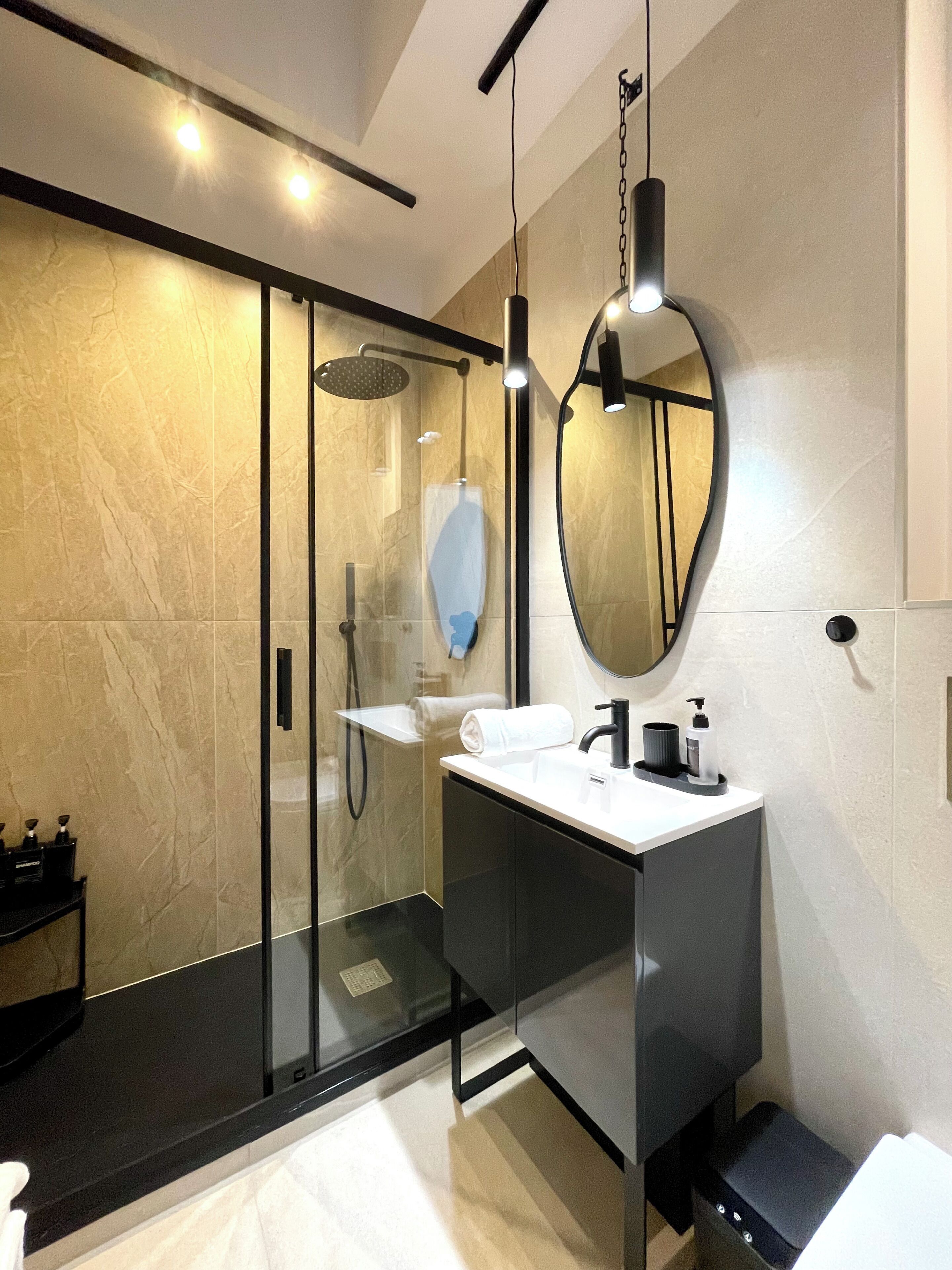A modern bathroom with a glass-enclosed shower, a large mirror, and a black vanity.