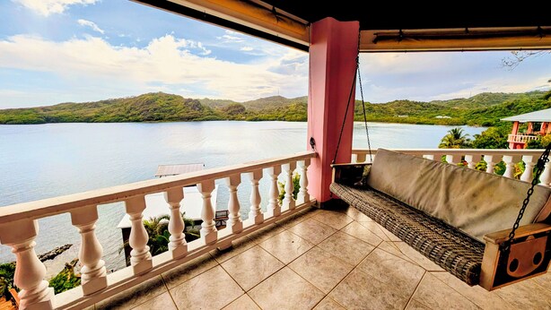 A balcony with a swing seat overlooking a lake and hills. - El Palacio Rosa - The Resort (Jose Santos Guardiola)