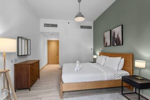 A modern hotel room with a wooden bed, a desk, a chair, a lamp, and artwork on the wall. - Spacious Designer 1BR in JVC (Dubai)
