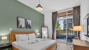 Ein Hotelzimmer mit Bett, Nachttischlampen, Schreibtisch, Stuhl, einem Balkon mit Aussicht und Kunstwerken an den Wänden.