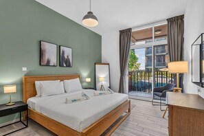 A hotel room with a bed, bedside lamps, a desk, a chair, a balcony with a view, and artwork on the walls. - Spacious Designer 1BR in JVC (Dubai)