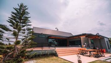 A modern building with a flat roof, large windows, and a covered outdoor seating area with tables and chairs.