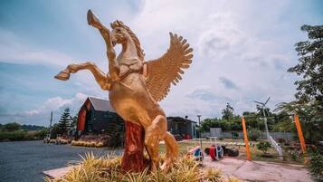 Une statue équestre dorée, représentant un cheval ailé, se trouve dans un espace paysager, avec un bâtiment en arrière-plan.