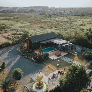 A modern house with a swimming pool, surrounded by a landscaped garden and a large tree. - KN Pool Villa Saraburi (Khok Yae)