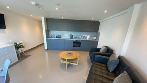 Een moderne woonkamer met een bank, een salontafel en een eethoek, met een keuken op de achtergrond.