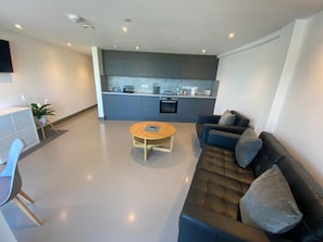 Ein modernes Wohnzimmer mit einer Couch, einem Couchtisch und einem Essbereich mit einer Küche im Hintergrund.