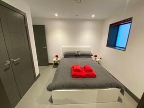 Ein modernes Schlafzimmer mit einem Bett, zwei Nachttischen, einem Fenster und einer Tür.