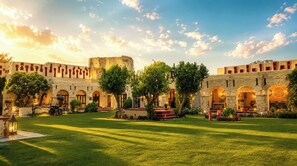 Un patio con edificios de piedra, paseos con arcos y vegetación.