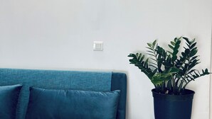 Ein Zimmer mit einem türkisblauen Sofa, einem Blumentopf und einem Wandschild mit Fischillustrationen und dem Text 'IA ORA NA'.