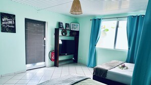Ein Zimmer mit Etagenbett, einem kleinen Tisch, einem an der Wand befestigten Regal mit Dekoration und einem Fenster mit Vorhängen.