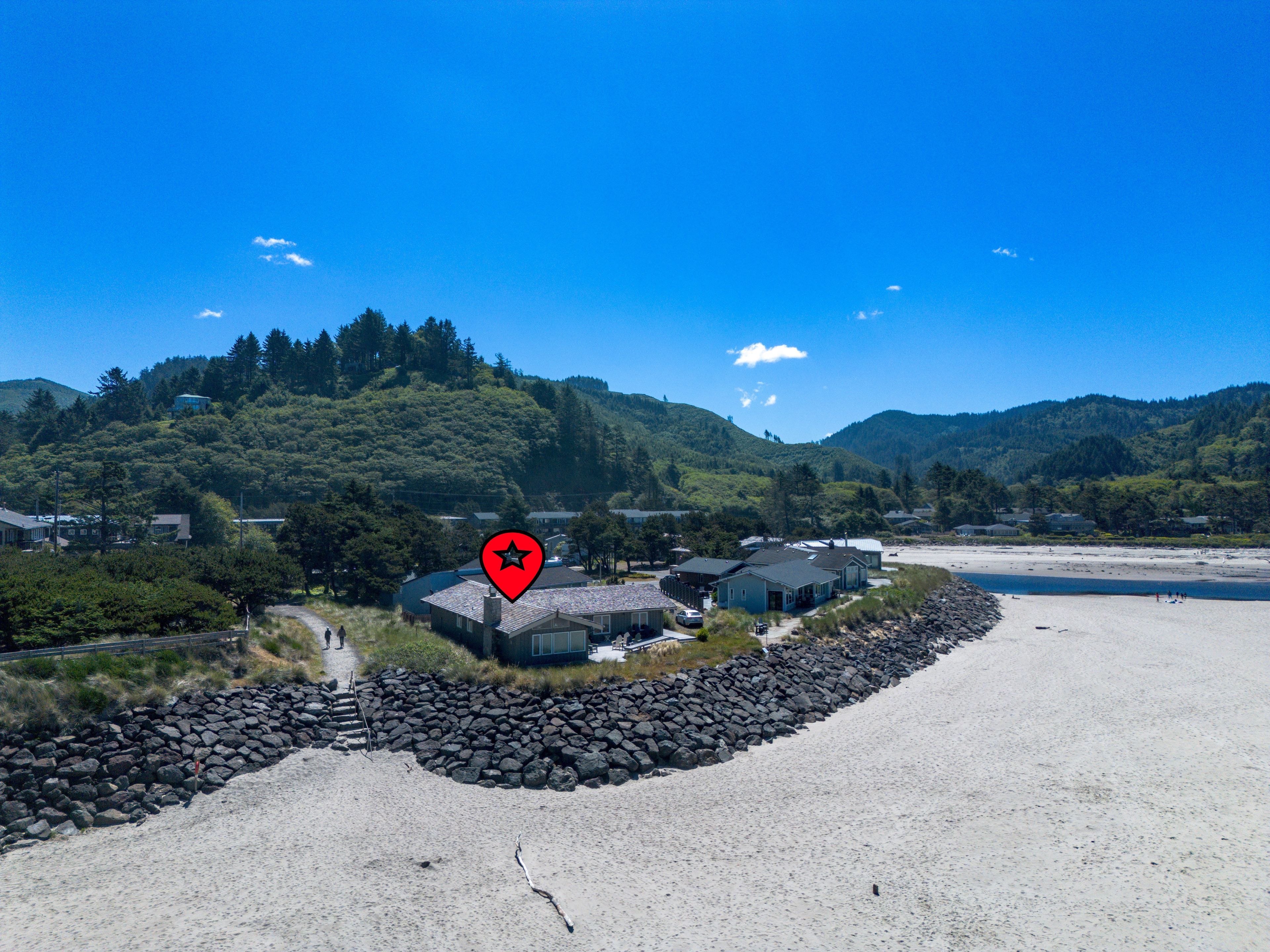 A coastal property with a beach, houses, and a forested hillside.