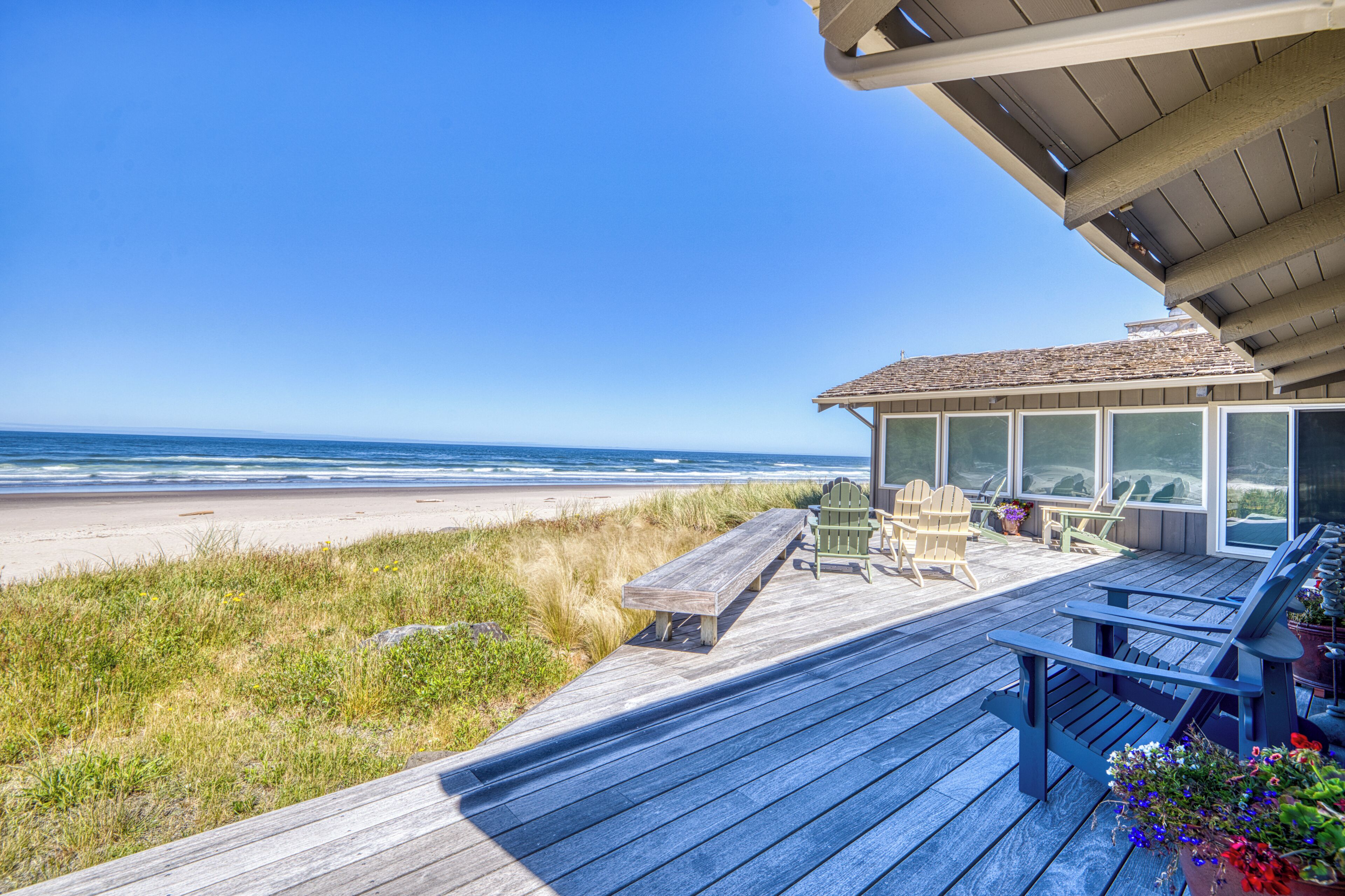 Terraza de madera con mobiliario exterior, con vistas a una playa.