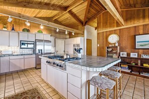 A kitchen with a large island, white cabinets, stainless steel appliances, and a wooden ceiling. - Nestle Inn-direct beach access, views, best spot in town. (Neskowin)