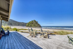 A wooden deck with Adirondack chairs and a picnic table overlooking a beach and forested island. - Nestle Inn-direct beach access, views, best spot in town. (Neskowin)