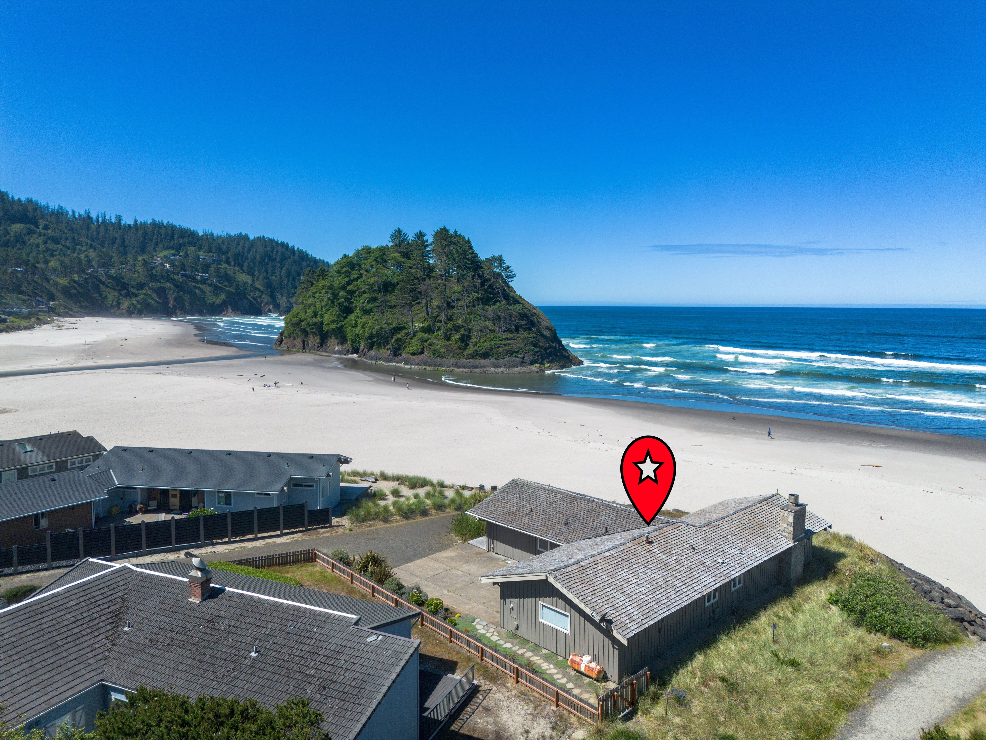 A coastal property with a beach view, a fenced yard, and a building with a sloped roof.
