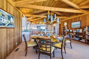 A spacious kitchen with modern appliances, a dining area with wooden chairs and a glass table, and a cozy living area with bookshelves and a painting. - Nestle Inn-direct beach access, views, best spot in town. (Neskowin)