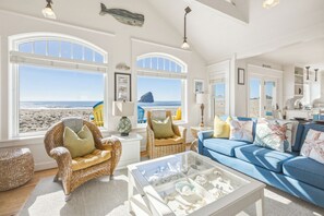Blick auf einen Strand von einem Zimmer aus, das Korbmöbel, einen Glastisch und ein blaues Sofa beherbergt.