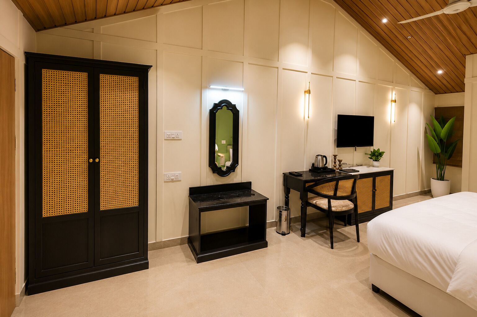 Una habitación de hotel con cama, escritorio, silla, televisor, espejo y planta.