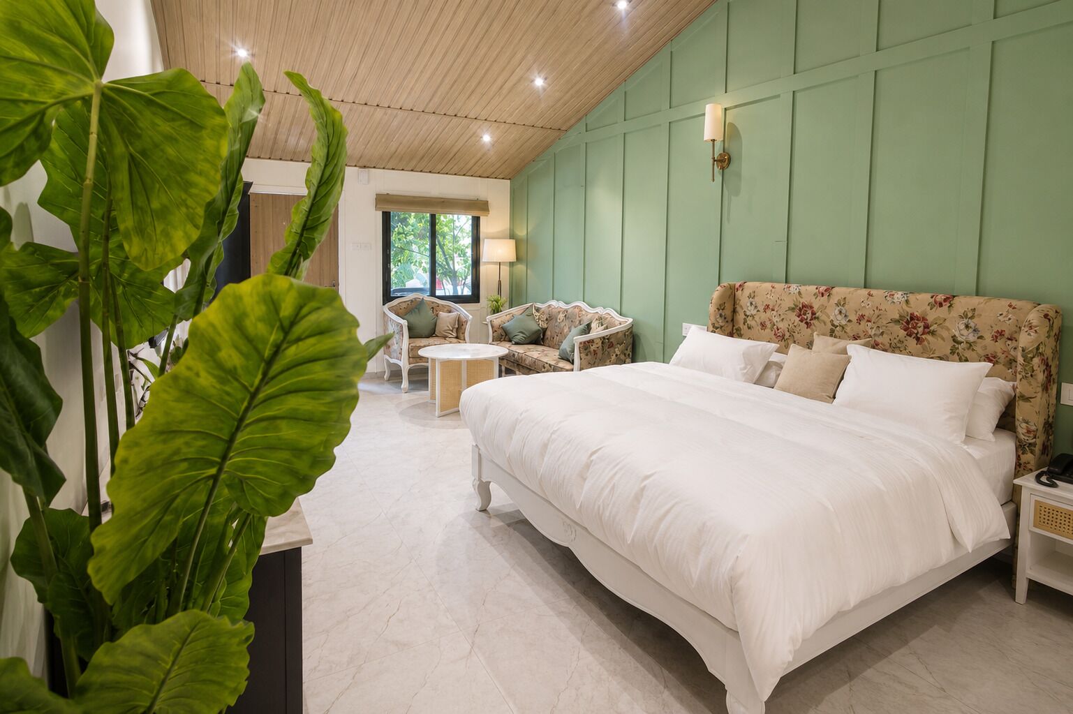 Un dormitorio con una cama grande, un sofá, una mesita y una planta en maceta.