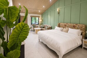 Un dormitorio con una cama grande, un sofá, una mesita y una planta en maceta.
