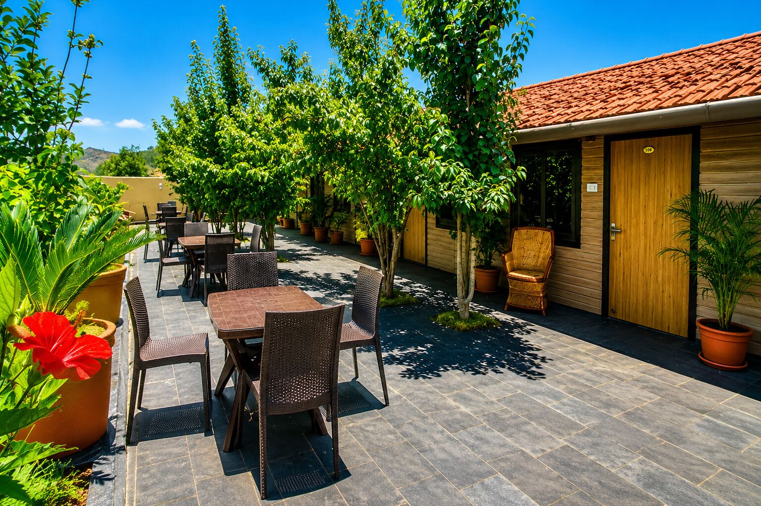 An outdoor patio with tables and chairs, surrounded by potted plants and trees.