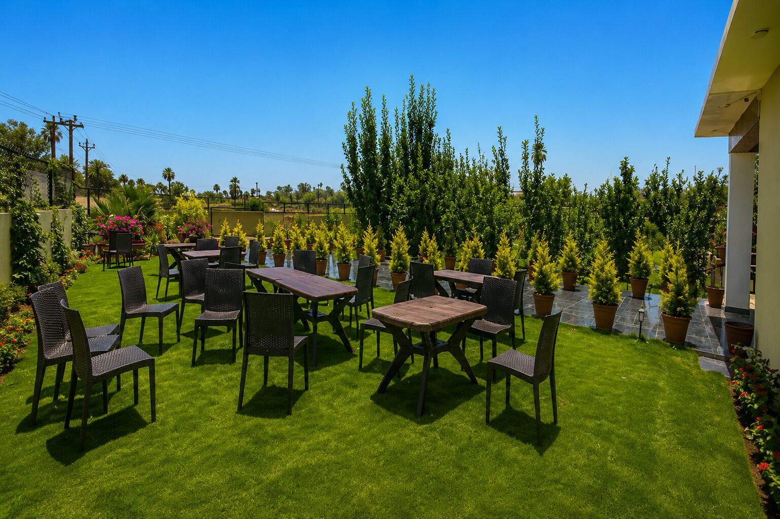 An outdoor patio with tables and chairs, surrounded by a well-maintained lawn and potted plants.