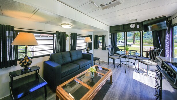 A hotel room with a sofa, a coffee table, a dining table with chairs, and a TV. - Fish, Hunt & Explore! Mtn-View Tiny Home in Noxon (Noxon)