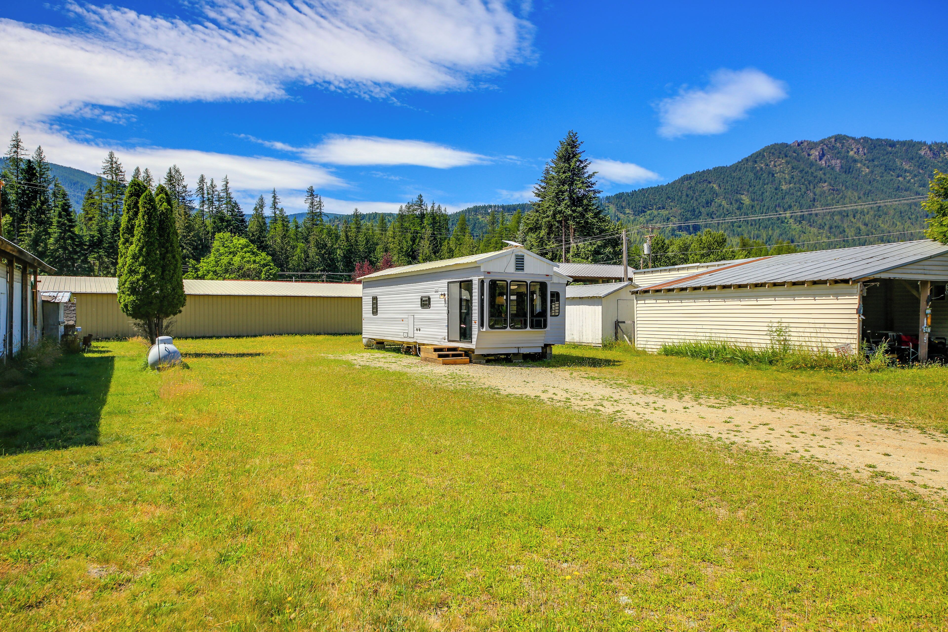 A mobile home with a large window, a small porch, and a dirt path leading to it.