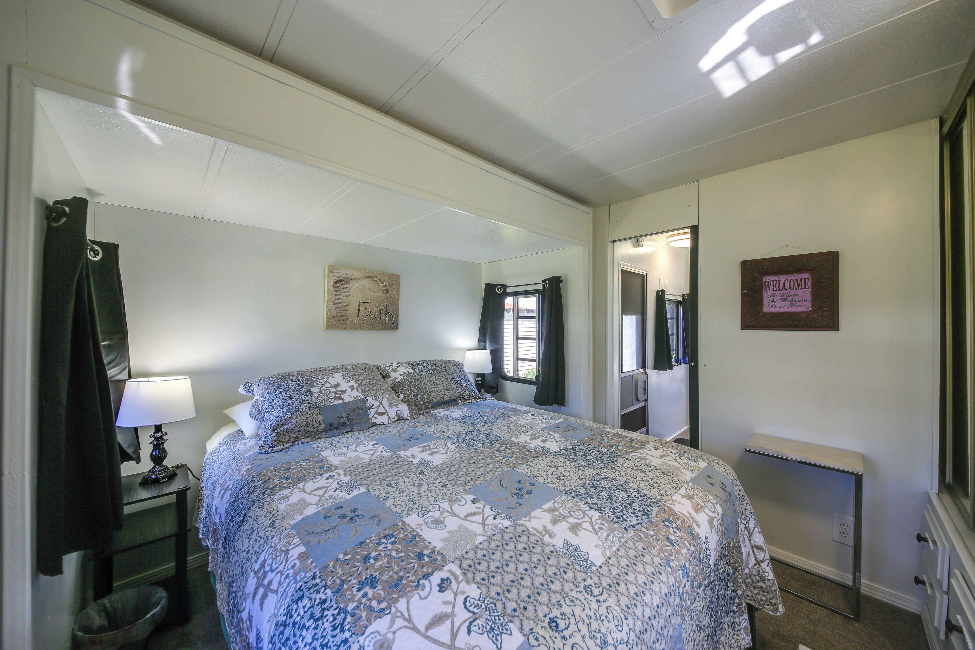 Une chambre à coucher avec un lit, une table de chevet avec une lampe, un miroir, un panneau d’accueil et une poubelle.